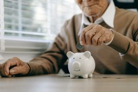 Rentner wirft eine Münze in ein Sparschwein